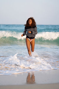 Woman with dark skin and long curly hair having fun at the beach running playing in the waves