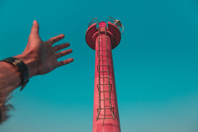 Cropped hand of man reaching tower against clear sky