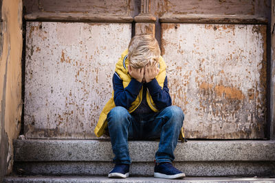 Tired boy sitting against weathered wall