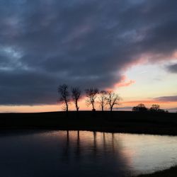 Silhouette trees by lake against sky during sunset