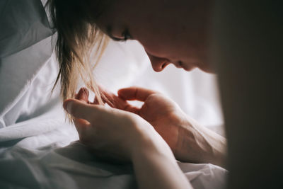 Close-up of woman looking at cupped hands on bed