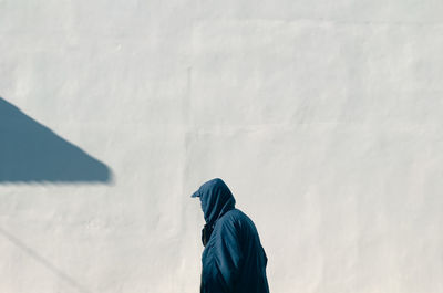 Man wearing hoodie standing against wall