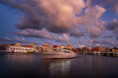 Illuminated buildings by river against sky in city