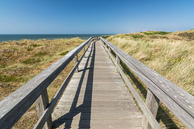 Boardwalk leading towards bridge against clear sky