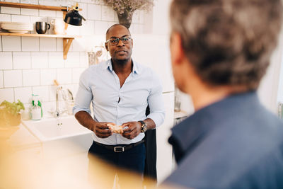 Man holding bread slice while talking to friend in kitchen at home