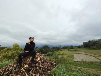 Man sitting on field against sky