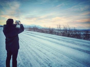 Man photographing on snow covered landscape against sky