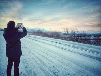 Person photographing on snow covered landscape against sky