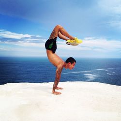 Full length of shirtless man jumping on beach against sky