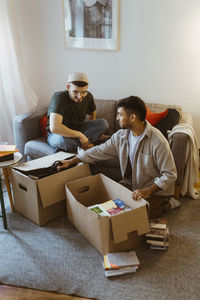 Gay couple talking to each other while unpacking cardboard boxes at home