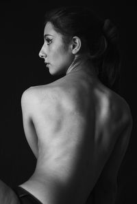 Side view of shirtless young woman looking away with black background