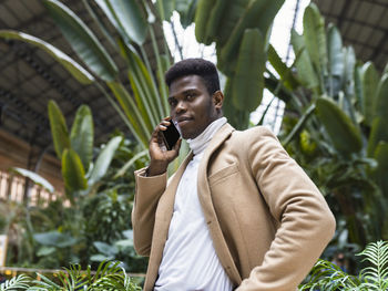 Young man using mobile phone while standing on plant