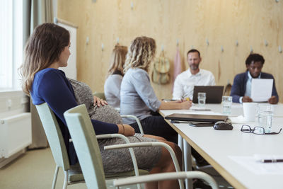 Pregnant executive looking at coworkers during meeting at office