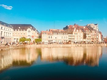 Reflection of buildings in lake against blue sky