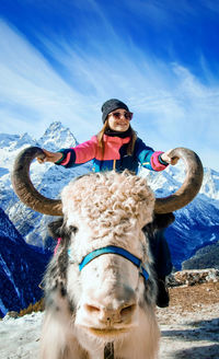 Smiling woman wearing knit hat sitting on highland cattle against sky