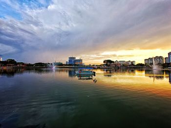 Scenic view of river by buildings against sky during sunset