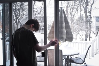 Side view of boy standing by window at home