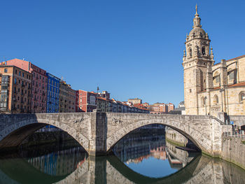 Arch bridge over canal amidst buildings against sky in city