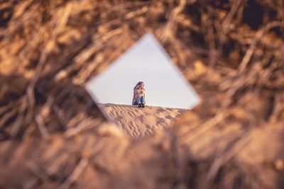 Reflection of woman sitting on sand in mirror