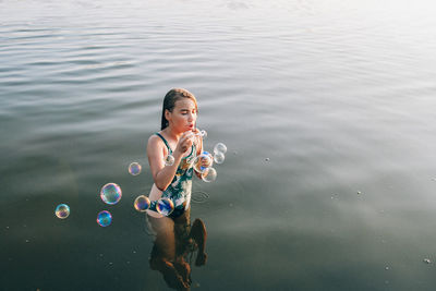 Teenage girl blowing bubbles while standing in lake