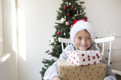 Portrait of happy boy holding gift box sitting against christmas tree