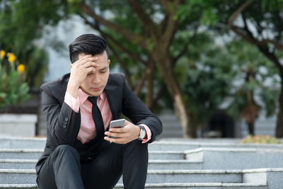 Depressed young businessman using mobile phone