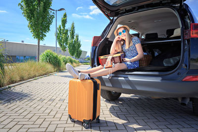 Portrait of teenage girl with guitar sitting in car trunk by luggage
