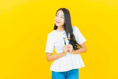 Portrait of smiling young woman standing against yellow background