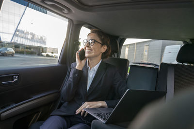 Smiling businesswoman talking on mobile phone in car