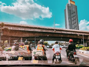 People riding bicycles on bridge in city against sky