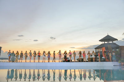 People looking at swimming pool against sky at sunset