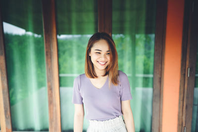 Thoughtful young woman smiling while standing against window