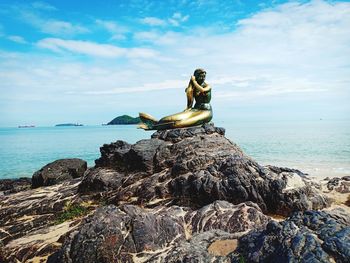 Statue on rock by sea against sky