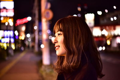 Smiling woman looking away in illuminated city at night