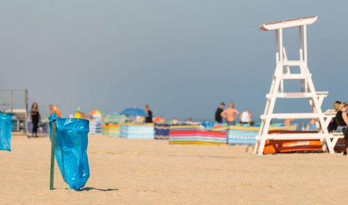 An empty garbage bag on the beach on a sunny summer day, in the background people, a beach screen