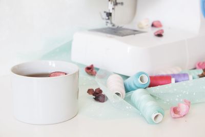 Close-up of sewing machine and thread spools against white background
