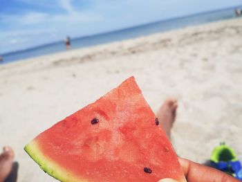 Close-up of hand holding fruit on sand at beach