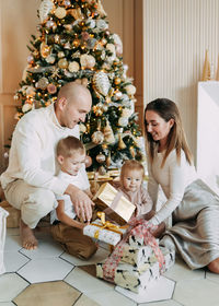 A family with children celebrate give gift boxes decorate a christmas tree in the interior the house