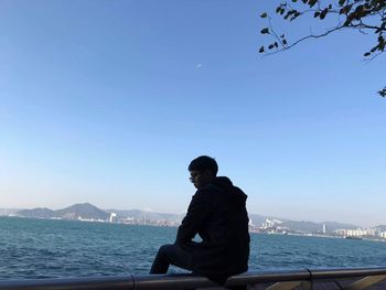 Rear view of man looking at sea against clear sky