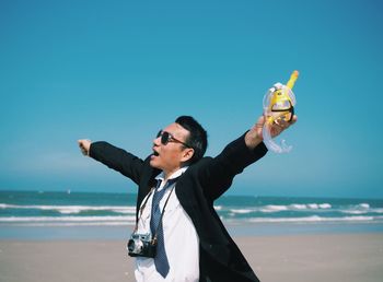 Young man with arms outstretched standing on beach