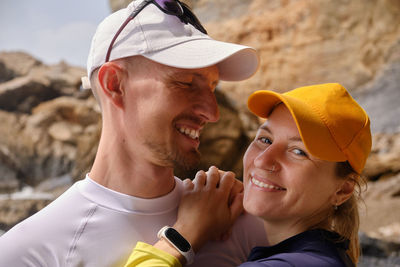 Young woman looks to camera and puts hands on her young man shoulder standing on a beach