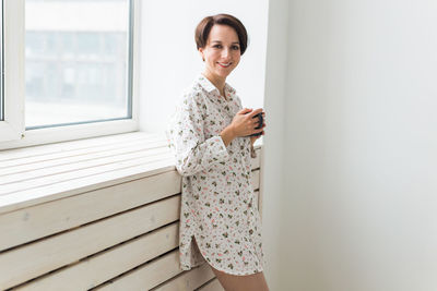 Portrait of a smiling young woman standing against wall