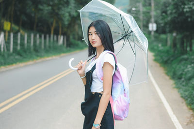 Woman holding umbrella while standing on road