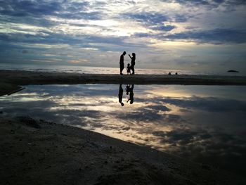 Silhouette family standing at beach against cloudy sky during sunset