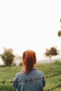 Rear view of woman looking at field against clear sky