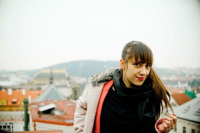 Portrait of smiling young woman in city against sky