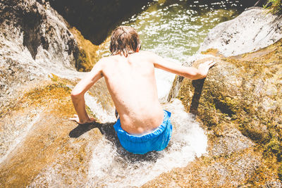 Rear view of shirtless young boys have fun at the small river outdoor summer activities