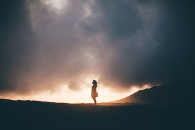 Silhouette woman standing on landscape against clouds