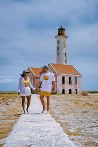 Rear view of people walking on road by lighthouse against sky