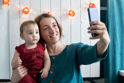 Mother and daughter making selfie in christmas decor. remote celebration. blogger creating stories. 